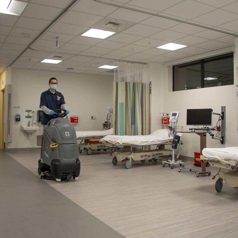 A masked, gloved 3Z's technician machine-scrubbing the floor of a medical facility
